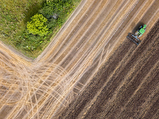 Image showing An agricultural field after harvesting with tractor plowing the soil on a summer day. Top view