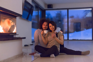 Image showing happy multiethnic couple sitting in front of fireplace