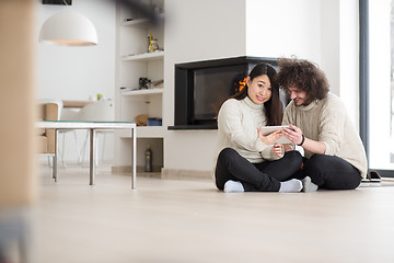 Image showing multiethnic couple using tablet computer in front of fireplace