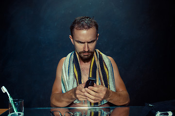 Image showing The young man in bedroom sitting in front of the mirror scratching his beard