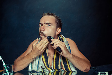 Image showing The young man in bedroom sitting in front of the mirror scratching his beard