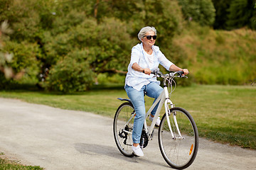 Image showing happy senior woman riding bicycle at summer park