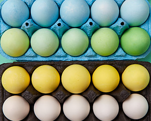 Image showing A collection of painted yellow, green, white and blue eggs in cardboard boxes. Creative Easter background. Flat lay