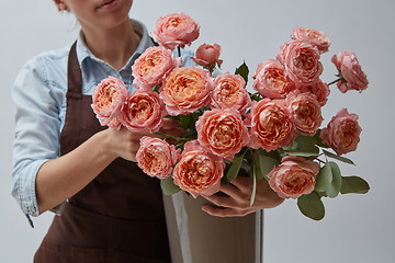 Image showing Female hands holding a vase with flowers of pink roses around a gray background. The concept of a flower shop