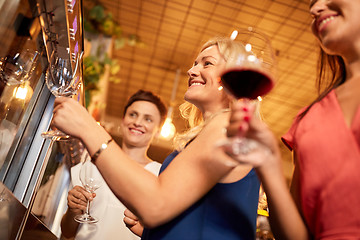 Image showing happy women pouring wine from dispenser at bar