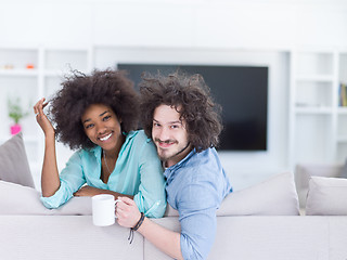 Image showing multiethnic couple sitting on sofa at home drinking coffe