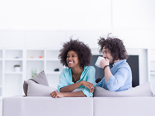 Image showing multiethnic couple sitting on sofa at home drinking coffe