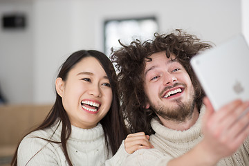 Image showing multiethnic couple using tablet computer in front of fireplace