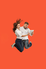 Image showing Image of young couple over red background using laptop computer or tablet gadget while jumping.