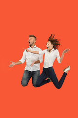 Image showing Freedom in moving. Surprised young couple jumping against red background