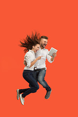 Image showing Image of young couple over red background using laptop computer or tablet gadget while jumping.