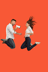 Image showing Beautiful young couple jumping with megaphone isolated over red background