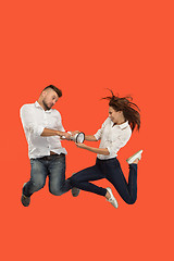 Image showing Beautiful young couple jumping with megaphone isolated over red background