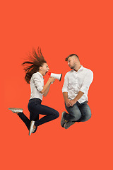 Image showing Beautiful young couple jumping with megaphone isolated over red background