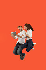 Image showing Image of young couple over red background using laptop computer or tablet gadget while jumping.