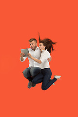 Image showing Image of young couple over red background using laptop computer or tablet gadget while jumping.