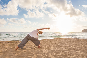 Image showing Woman practicing yoga on sea beach at sunset.