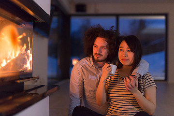 Image showing happy multiethnic couple sitting in front of fireplace