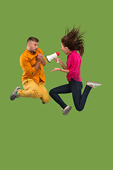 Image showing Beautiful young couple jumping with megaphone isolated over green background