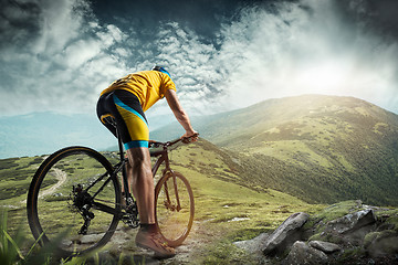 Image showing The young fit men in helmet conquering mountains on a bicycle.