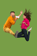 Image showing Beautiful young couple jumping with megaphone isolated over green background