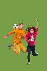 Image showing Forward to the victory.The young couple as soccer football player jumping and kicking the ball at studio on a green