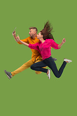 Image showing Jump of young couple over green studio background using laptop or tablet gadget while jumping.