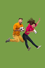 Image showing Forward to the victory.The young couple as soccer football player jumping and kicking the ball at studio on a green