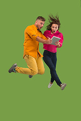 Image showing Jump of young couple over green studio background using laptop or tablet gadget while jumping.