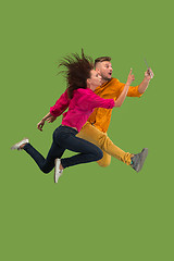 Image showing Jump of young couple over green studio background using laptop or tablet gadget while jumping.