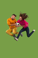 Image showing Forward to the victory.The young couple as soccer football player jumping and kicking the ball at studio on a green