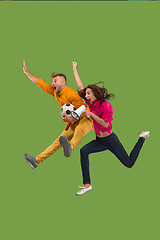 Image showing Forward to the victory.The young couple as soccer football player jumping and kicking the ball at studio on a green