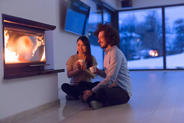 Image showing happy multiethnic couple sitting in front of fireplace