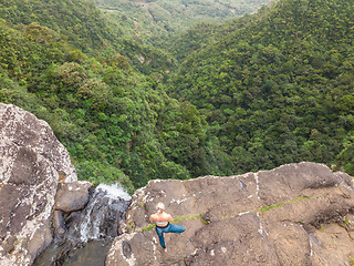 Image showing Active sporty woman relaxing in nature, practicing yoga on high clif by 500 feet waterfall at Black river gorges national park on tropical paradise island of Mauritius