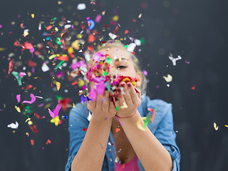 Image showing woman blowing confetti in the air isolated over gray