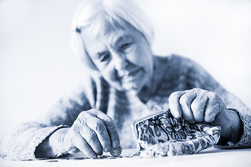 Image showing Concerned elderly woman sitting at the table counting money in her wallet. Black and white blue toned image.