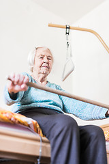 Image showing Elderly 96 years old woman exercising with a stick sitting on her bad.