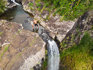 Image showing Aerial top view of travel couple waving to drone, standing on the edge of 500 feet waterfall in the tropical island jungle of Black river gorges national park on Mauritius island