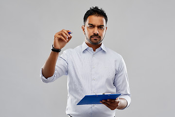 Image showing strained indian businessman writing to clipboard