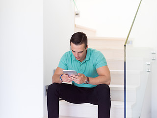 Image showing man using a tablet while sitting on the stairs at home