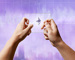 Image showing A man holds a glass screen with Icons of ethereum and a crypto currency graph