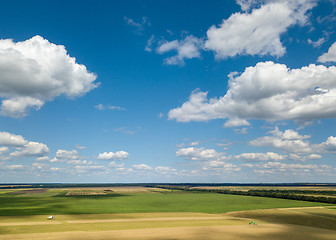 Image showing Panoramic view from the drone of beautiful landscape of agricultural fields with harvesting on the background of the blue cloudy sky at sunset.