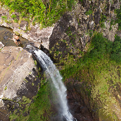 Image showing Aerial top view of travel couple waving to drone, standing on the edge of 500 feet waterfall in the tropical island jungle of Black river gorges national park on Mauritius island