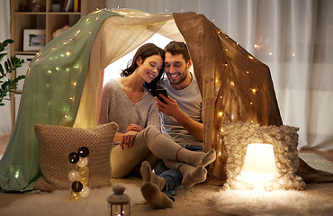 Image showing happy couple with smartphone in kids tent at home