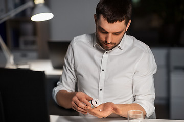 Image showing businessman taking medicine pills at night office