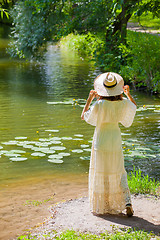 Image showing girl in a white dress and hat on the shore of a pond with water-