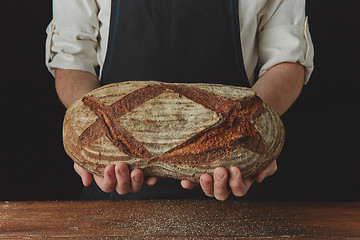 Image showing Baker\'s hands hold an oval bread.