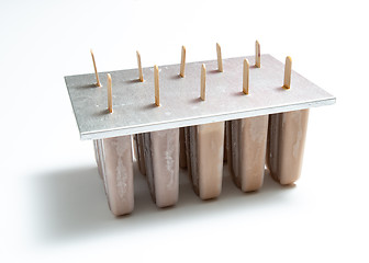 Image showing Homemade organic chocolate ice cream lolly in plastic molds with a reflection of shadows on a white background with copy space.