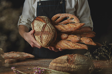 Image showing Baker in black apron holds variety of bread