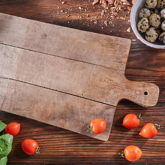 Image showing Ripe tomatoes, quail eggs in a bowl and nut crumbs on a wooden board with a toe with an empty board and copy space. Salad preparation concep. Top view